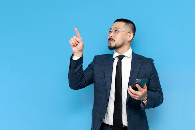 Asian businessman in suit and glasses holds smartphone and presses with finger on an empty space