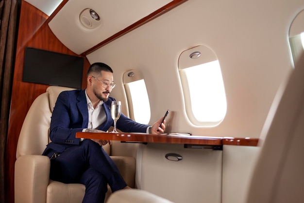 asian businessman in suit and glasses with glass of champagne flies in private luxury jet