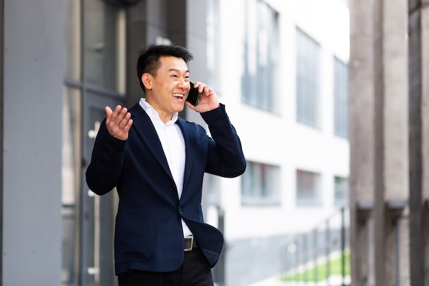 Asian businessman talking on the phone cheerful smiling reports good news near the office center outside