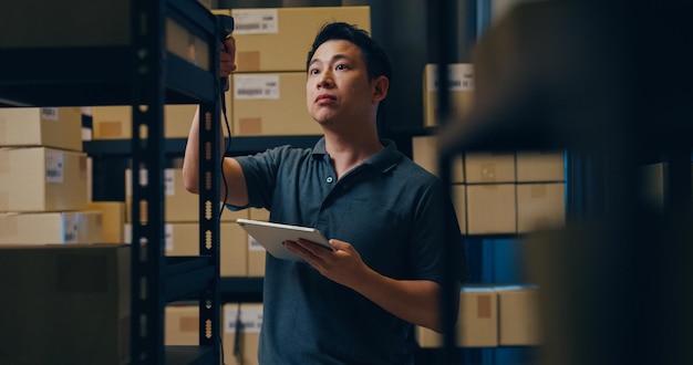 写真 アジアのビジネスマンはバーコード スキャナーを使用して棚の紙箱をスキャンし、デジタル タブレットにデータを置き、倉庫で速達するためのオンライン データ情報の詳細をカットストックします。スタートアップ中小企業のコンセプト