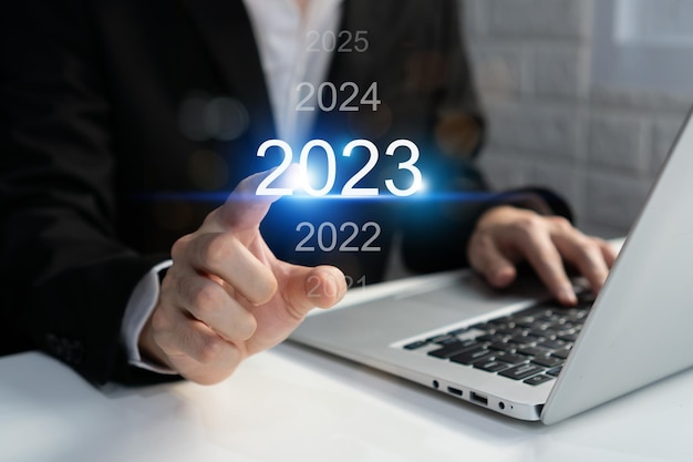 Asian businessman using computer with virtual 2023 year diagram Business planning trend change from 2022 to 2023 goals strategy investment Happy new year concept Closeup and copy space