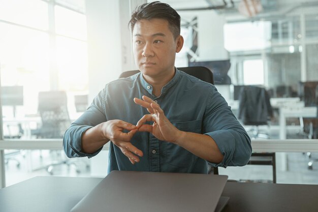 Asian businessman using sign language with colleagues and\
friends while sitting in office