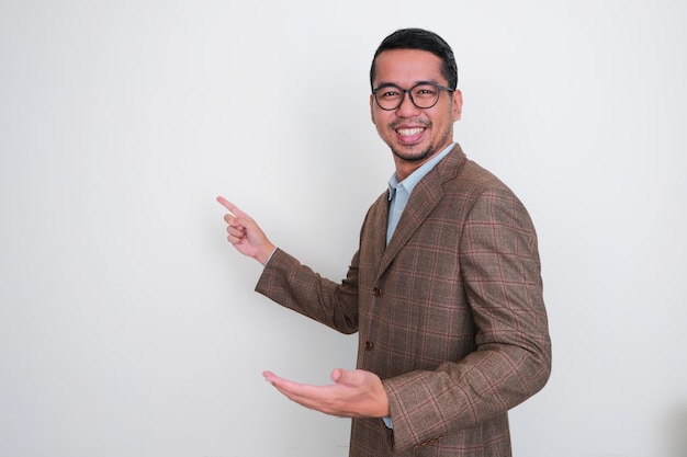 Азиатский бизнесмен в коричневом костюме счастливо улыбается, указывая пальцем на пустое пространство позади