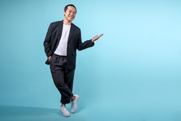 Asian businessman wearing semiformal suit and presenting gesture to empty space on blue background
