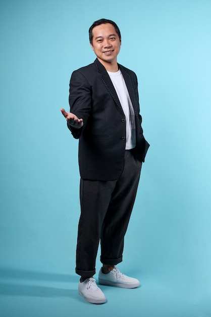 Азиатский бизнесмен в полуформальном костюме с презентационным жестом, изолированным на синем фоне