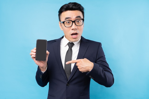 Asian businessman wearing suit holding smartphone on blue wall