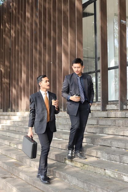 Asian businessman wearing suits are walking together  while having informal discussion outdoors