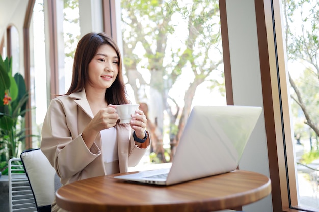 コーヒーを飲み、コーヒーショップでラップトップで作業するカジュアルなスーツを着たアジアの実業家