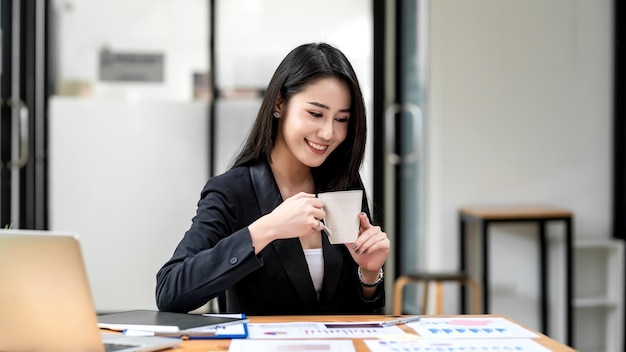 Asian businesswoman drinking coffee happy success at work document graph tablet placed at the office.