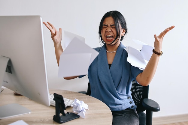 Asian businesswoman or female office worker screaming shouting and throwing up papers at her office