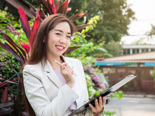 Asian businesswoman holding documents file standing outdoors. Smiling successful young businesswoman.