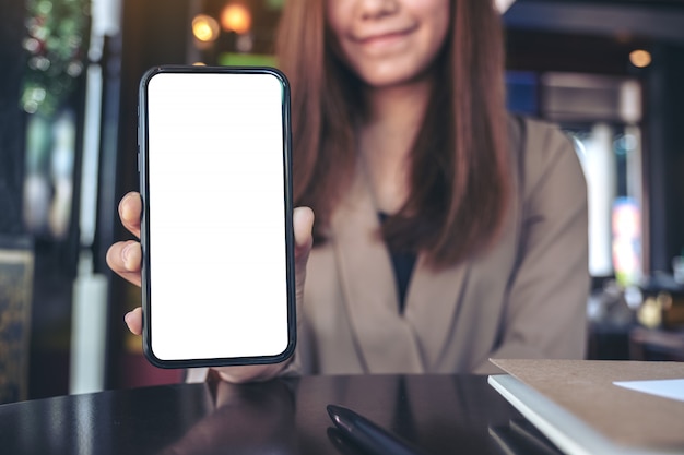  an asian businesswoman holding and showing black mobile phone with blank white screen in cafe