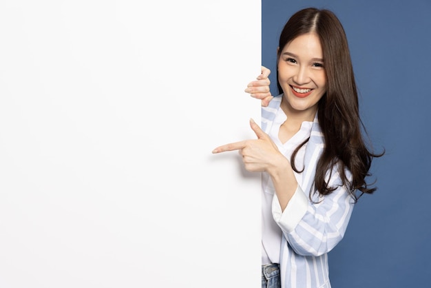 Photo asian businesswoman is standing behind the white blank banner on blue background