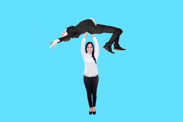 Asian businesswoman lifting caucasian businessman isolated on blue background