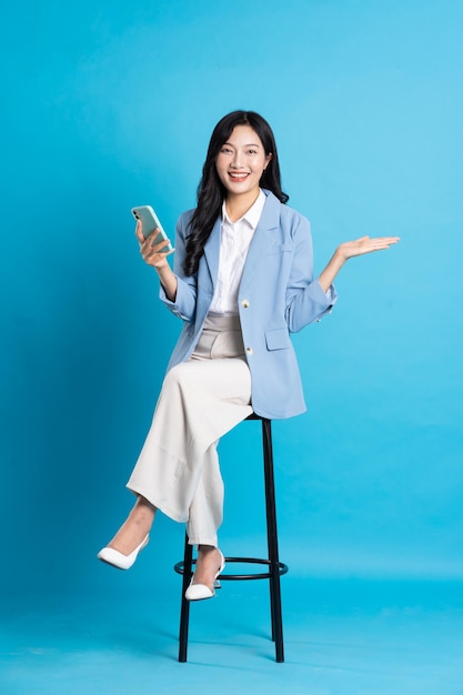 Asian businesswoman portrait sitting on chair isolated on blue background