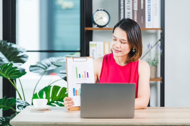 Asian businesswoman presenting business report via video call on a laptop at home. Businessperson or entrepreneur working, online shopping, e-commerce, internet banking, working from home concept