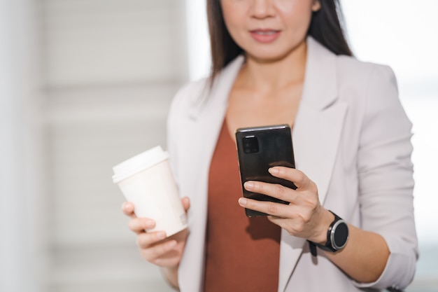 Una donna d'affari asiatica in un completo rilassato tiene una tazza di caffè da asporto in un edificio aziendale