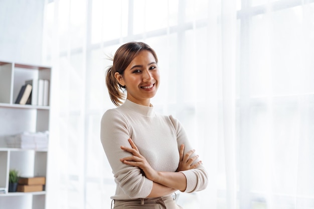Азиатская деловая женщина, стоящая со скрещенными руками на рабочем месте в офисе