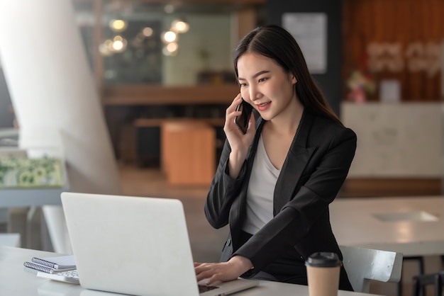 Donna d'affari asiatica che parla al telefono con i clienti pronti a utilizzare un laptop in ufficio.