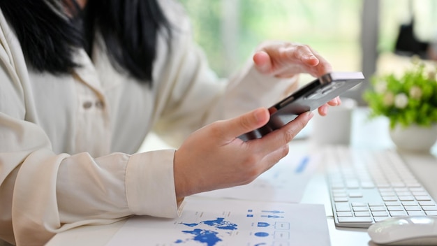 An Asian businesswoman using her smartphone at her desk cropped image