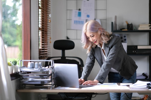 Asian Businesswoman Using laptop computer and working at office with calculator document on desk doing planning analyzing the financial report business plan investment finance analysis concept