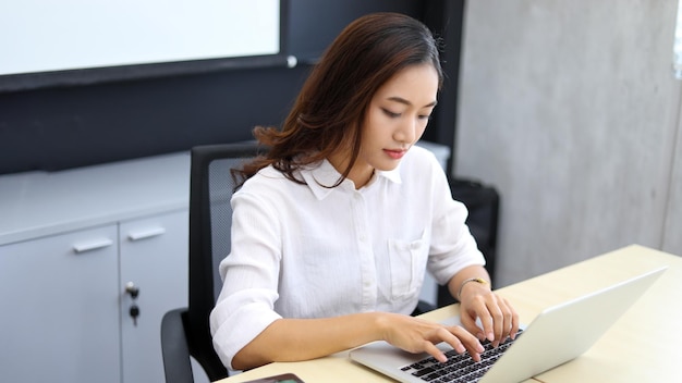 Donna d'affari asiatica che utilizza il laptop per lavoro e fa ricerche su internet nel suo ufficio