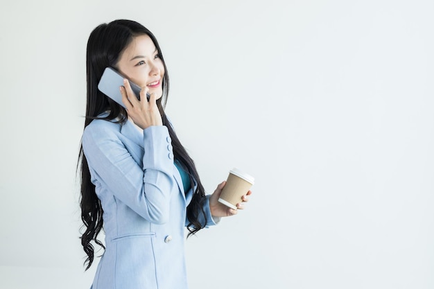 Asian businesswoman using mobile phone while holding cup of coffee Business finance and employment female successful entrepreneurs Smiling pleasant asian businesswoman