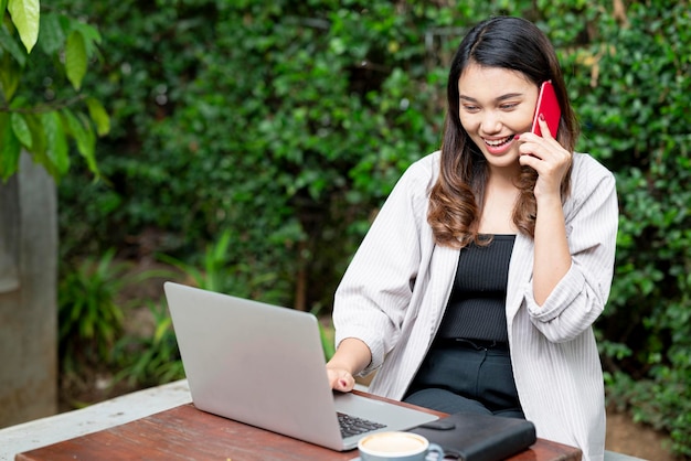 Asian businesswoman using a mobile phone with laptop notebook and cup of coffee on the table