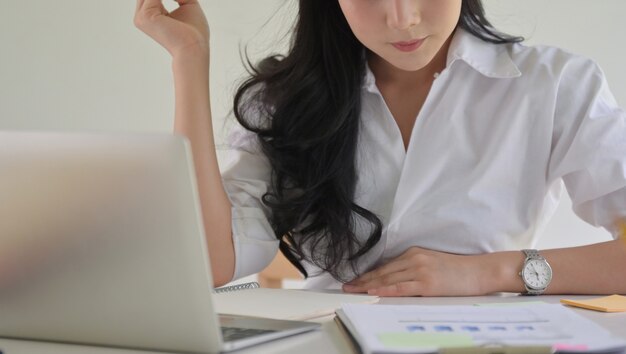 La donna di affari asiatica con una penna a disposizione sta controllando le prestazioni dell'azienda.