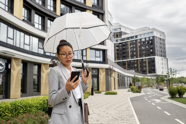 Asian businesswoman with umbrella scrolling in smartphone