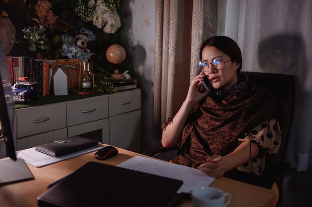 アジアの実業家は夜に残業します。働く女性のライフスタイル。同僚とのオンラインコミュニケーションとビデオ会議。社会的距離と新しい正常。