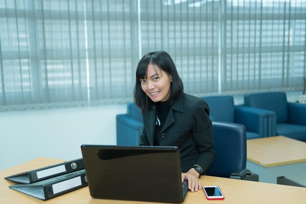 Азиатская деловая женщина, работающая за столом в офисеУлыбка работницы из ТаиландаКрасивый секретарь имеет приятную улыбкуЛеди клерк сверхурочно в компании