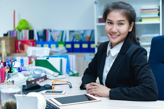 オフィスの机で働くアジア人実業家タイ人労働者女性smileBeautiful秘書が素敵な笑顔を持っている会社で残業中の女性事務員