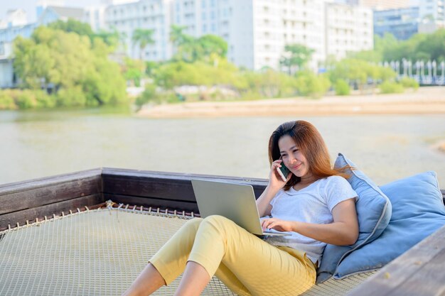 Asian businesswoman working online at the beach. Freelancer using technology for work everywhere. Woman talking with customer with mobile phone.