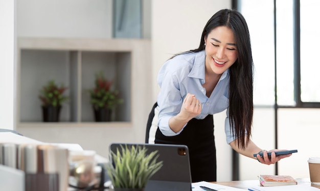 Asian businesswomen show joyful expression of success at work smiling happily with a laptop computer in a modern office