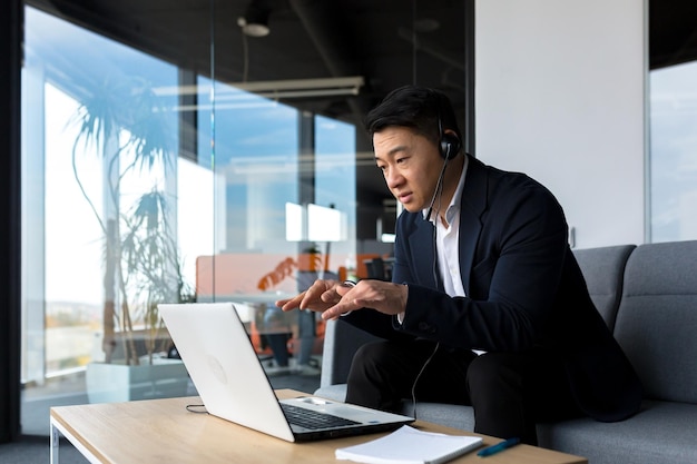 Asian call center employee talking to customers sitting in office Asian businessman using headset and laptop for video call happy and smiling