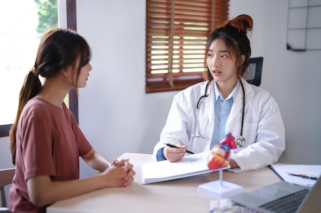 Photo asian cardiologist doctor women pointing on document to explaining about health examination results to female patient while giving counseling about medical and mental health therapy in clinic