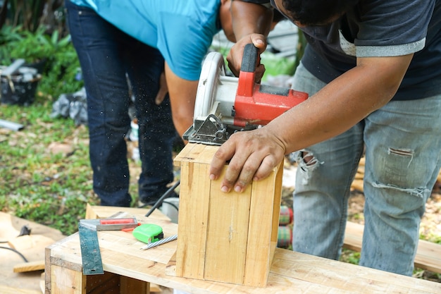 Asian carpenter are sawing the wood in the backyard garden at home.