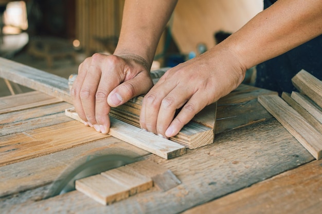 Asian carpenter is using a circular saw to cut wood to\
construct a storage box on a desk table at his factory working as\
your own boss at home concept