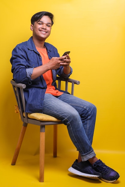 Asian cheerful young man using smart phone sit on chair and looking at camera smiling