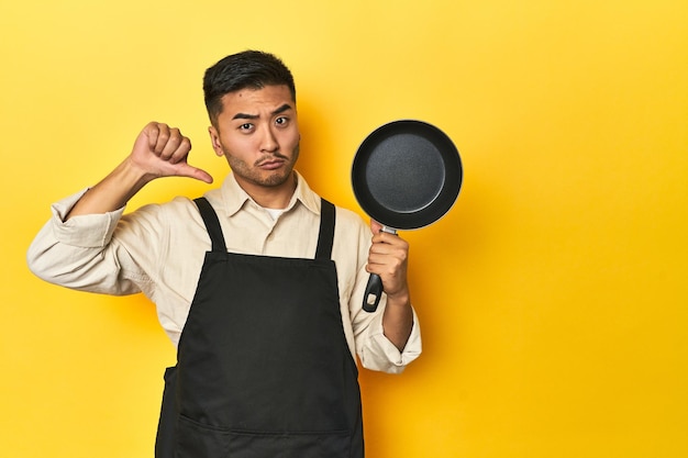 Photo asian chef holding a pan yellow studio backdrop feels proud and self confident example to follow