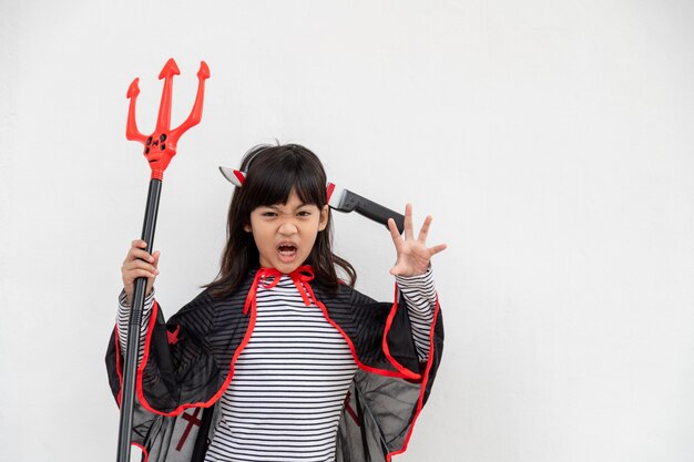 Photo asian child girl in demon costume holding black and red trident, happy halloween concept