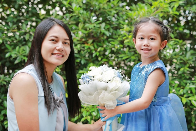 Asian child girl giving bouquet of flowers for her mother in the garden.