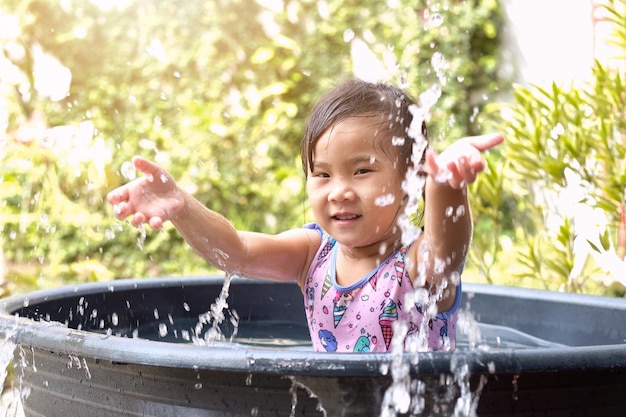 アジアの子供の女の子は,盆で水を遊んでいる間,庭で幸せな女の子に水を打った.