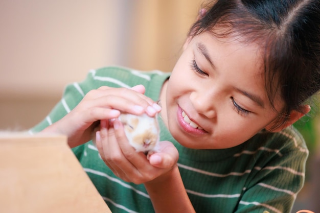 Asian child girl holding tiny bunny in hand with tenderness and love Kid take care a pet and decorate home for Easter Happy Easter Happy holiday