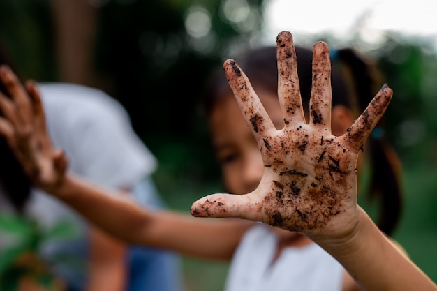 Photo asian child girl showing dirty hands after planting the tree in the garden