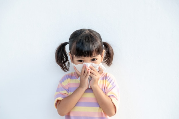 ほこりの天気や幼稚園、幼稚園からの弱いまたはウイルスや細菌のために鼻にくしゃみをし、ティッシュペーパーに冷たい咳をするアジアの子供の女の子