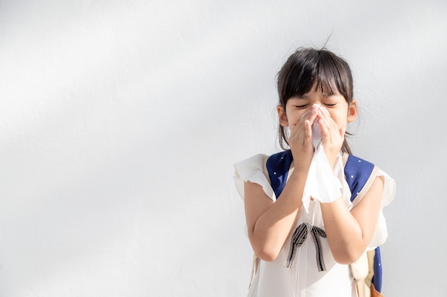 弱いので、鼻にくしゃみをし、ティッシュペーパーに風邪をひいて病気のアジアの子供の女の子