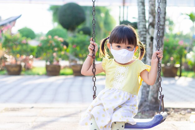 Asian​ child​ girl​ wearing​ a​ fabric​ face​ mask​ when​ she​ playing​ a​ toy​ at​ the​ playground.​