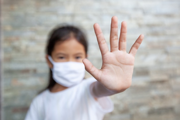 保護マスクを身に着けているアジアの子供女の子と停止コロナウイルスの発生のための停止手ジェスチャーを示します。彼女は、コロナウイルスcovid-19と大気汚染pm2.5から自宅で隔離しています。